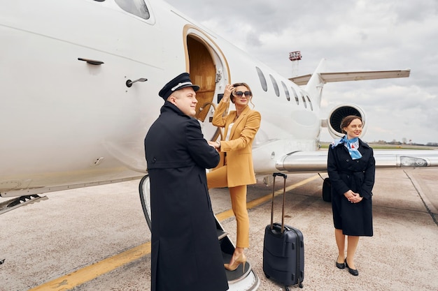 Vliegtuigbemanning leidt vrouw in gele kleren in vliegtuig
