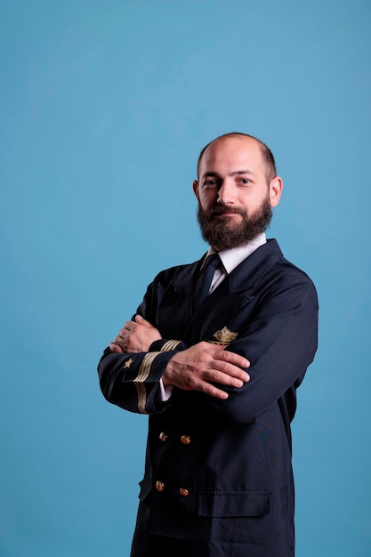 Vliegtuigpiloot met uniform portret staand met gekruiste armen, zelfverzekerde vliegtuigkapitein kijkend naar camera, studio-opname. Serieuze burgervlieger met badge op professioneel pak