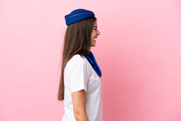 Vliegtuigstewardess Braziliaanse vrouw geïsoleerd op roze achtergrond lachen in laterale positie