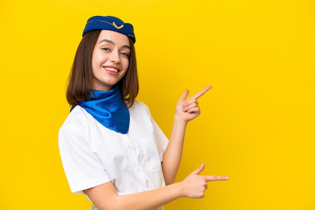 Vliegtuigstewardess Oekraïense vrouw geïsoleerd op gele achtergrond wijzende vinger naar de zijkant en een product presenteren