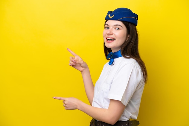 Vliegtuigstewardess Russische vrouw geïsoleerd op een gele achtergrond die met de vinger naar de zijkant wijst en een product presenteert