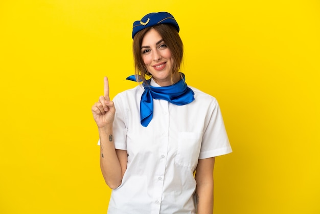 Vliegtuigstewardessvrouw geïsoleerd op gele achtergrond die een vinger toont en opheft in teken van de beste