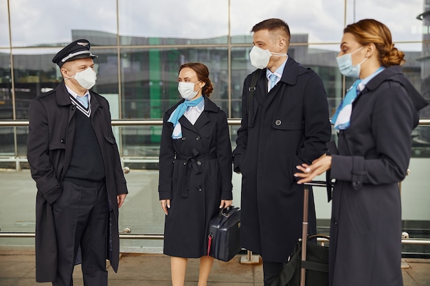 Vliegtuigteam staat en praat in de buurt van de luchthaven. vrouwen en mannen met bagage dragen uniforme en medische maskers. piloot, stewardess en stewardessen. teamwerk. burgerluchtvaart. vliegreisconcept