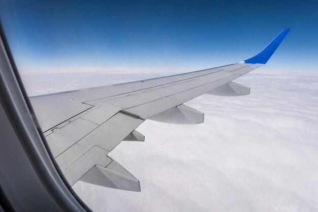 Vliegtuigvleugel vanuit het vliegtuigraam met uitzicht op de blauwe lucht en prachtige wolken
