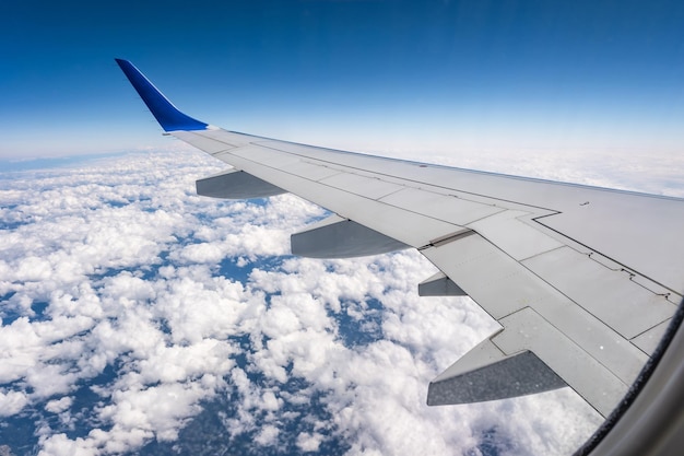 Vliegtuigvleugel vanuit het vliegtuigraam met uitzicht op de blauwe lucht en prachtige wolken