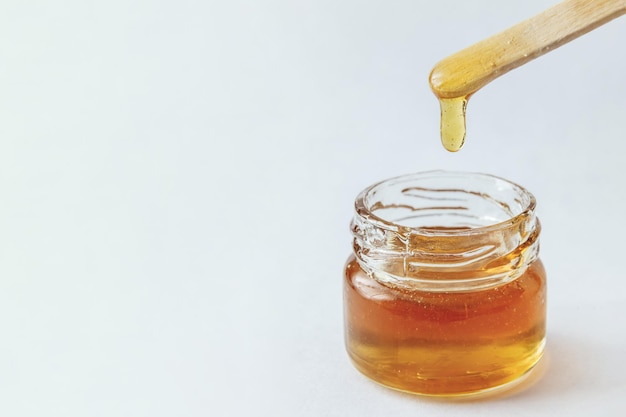 Vloeibare gele suikerpasta in glazen pot houten spatel op een witte achtergrond die honingvoedsel suikert