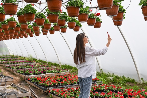 Vlog-opname van vrouwelijke bloemist jonge vrouw die een foto maakt van planten in een kas draadloos tuinieren