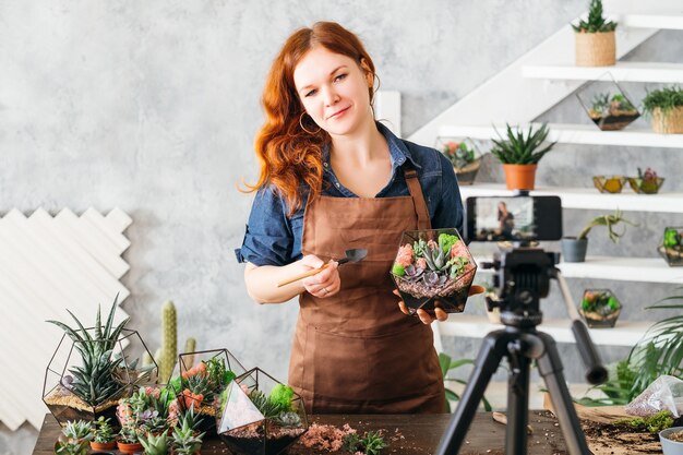 Vlog van natuurdecorspecialist. Vrouw die op smartphonecamera laat zien hoe je florarium maakt met vetplanten.