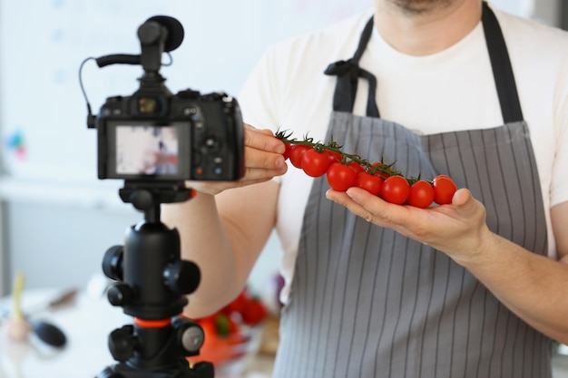 赤い野菜を記録するエプロンで完熟トマトの材料の男を示すVloggerシェフ