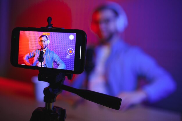 Foto vlogger gebruikt smartphone om podcast te filmen in studioblogger met microfoon van mobiele telefoon en koptelefoon die video filmt voor uitzendcarrière op sociale media