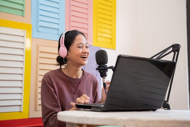 A vlogger girl is recording a podcast with a microphone and a computer laptop