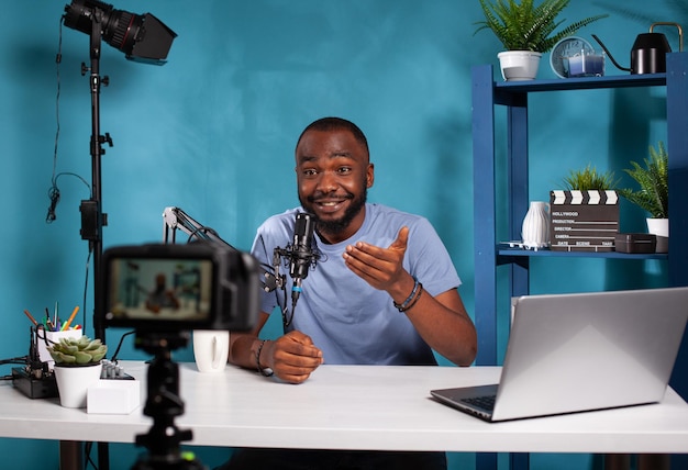 Vlogger talking with audience in excitement in front of recording digital video camera during online live show. Exalted content creator in studio looking at dslr live video podcast setup gesturing.