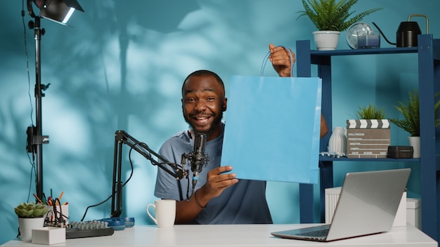 Vlogger toont papieren zak met cadeau aan camera in studio