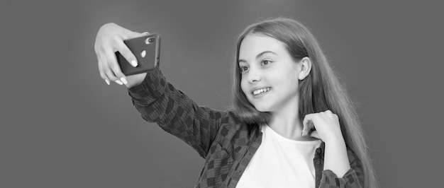 Vlogger with cellphone in classroom making video blog on smartphone teen girl blogging on phone back to school kid influencer or advisor smiling child making selfie school blogger