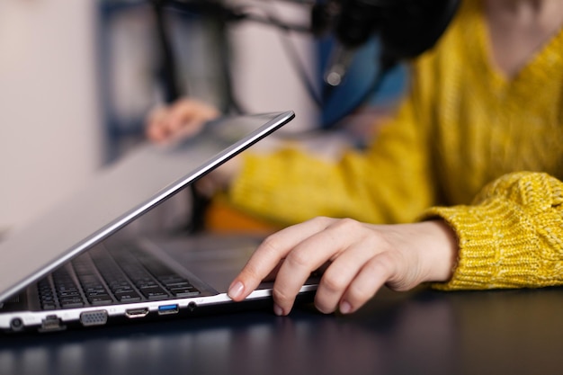 Vlogger woman opening laptop talking into professional microphone recording online podcast sitting at desk in podcasting studio at home. Social media influencer podcasting on-air studio