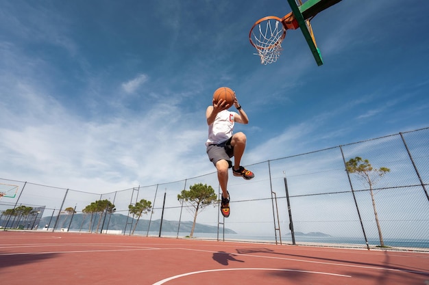 Vlore ALBANIA MAY 20 2022 Male basketball player shooting a jump shot outdoors Playing ball alone Sunrise ocean background