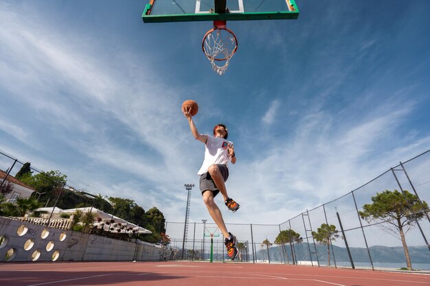 Vlore albania 20 maggio 2022 giocatore di basket maschile che spara un tiro in sospensione all'aperto giocando a palla da solo sunrise sullo sfondo dell'oceano