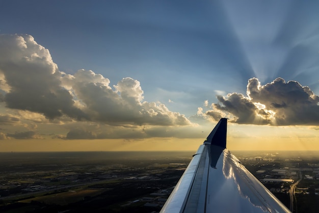 Vluchtvliegtuig van vleugel over dramatische witte pluizige wolken op blauwe lucht tijdens zonsondergang