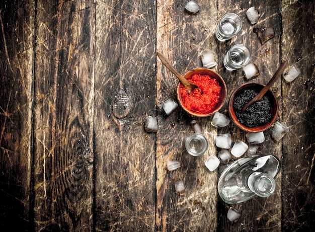 Vodka in a bottle with black and red caviar. On wooden background.