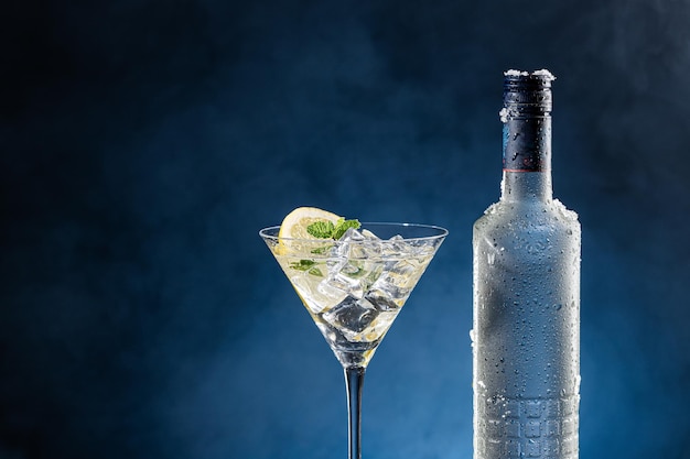 Vodka-cocktailglas en ijskoude fles op blauwe achtergrond met kopieerruimte