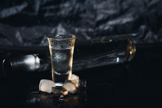 Vodka in shot glasses on black background, iced strong drink in misted glass