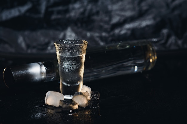 Photo vodka in shot glasses on black background, iced strong drink in misted glass