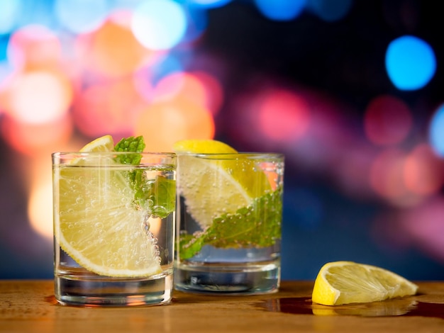 Vodka shot with fresh lemon and mint leaf in glass on bokeh background, Nightlife concept.