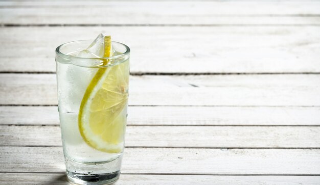 Photo vodka shots with lemon and ice. on a white wooden table.