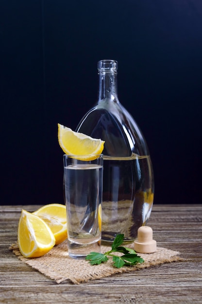 Vodka or tequila in shot glasses and in the bottle with lemon sliÑe on rustic wooden background.