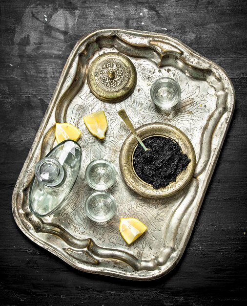 Vodka with caviar on the old tray. On a black chalkboard.