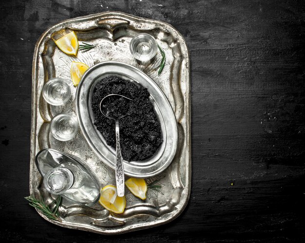 Vodka with caviar on old tray on black chalkboard.