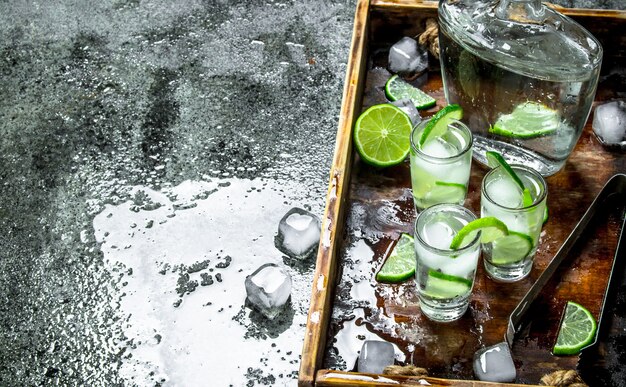 Vodka con lime e ghiaccio su un vassoio di legno. su fondo rustico.