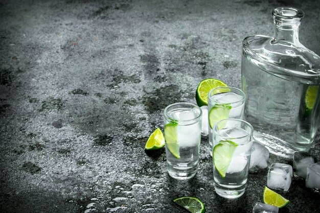 Vodka with pieces of lime and ice cubes. On a rustic background