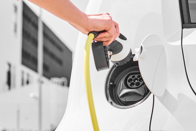 Voeding elektrische auto opladen op lader. Close-up van vrouw hand een oplader plug invoegen op elektrisch voertuig.