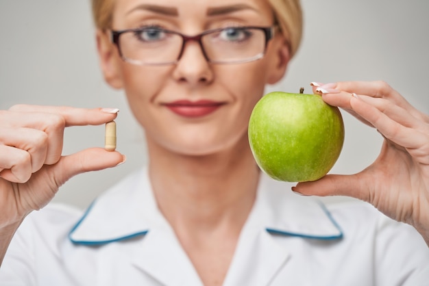 voedingsdeskundige arts gezonde levensstijl concept - biologische verse groene appel en vitamine capsules te houden