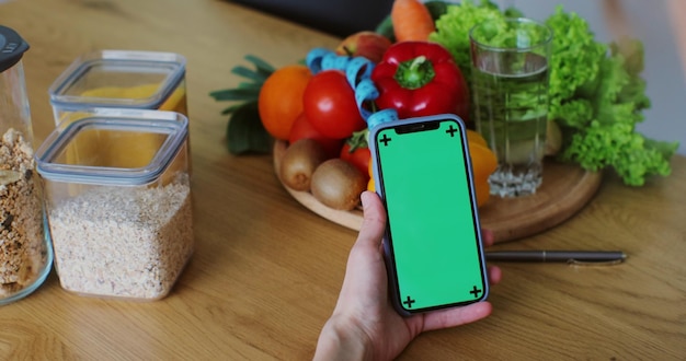 Voedingsdeskundige vrouw met gezonde groenten en fruit met behulp van smartphone met groen scherm Eenvoudig aanpasbaar groen scherm Juiste voedings- en dieetconcept
