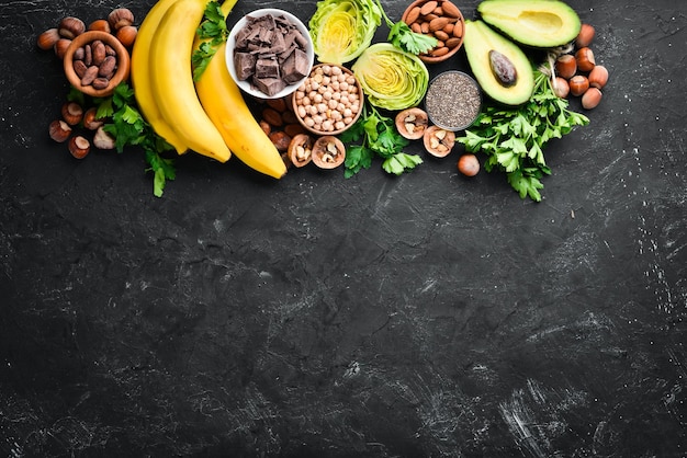 Voedingsmiddelen die natuurlijk magnesium bevatten Mg Chocolade Banaan Cacao Noten Avocado's Broccoli Amandelen Bovenaanzicht Op een zwarte achtergrond