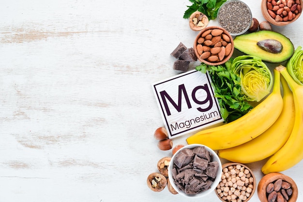 Voedingsmiddelen die natuurlijk magnesium Mg Chocolade Banaan Cacao Noten Avocado's Broccoli Amandelen Bovenaanzicht Op een witte houten achtergrond