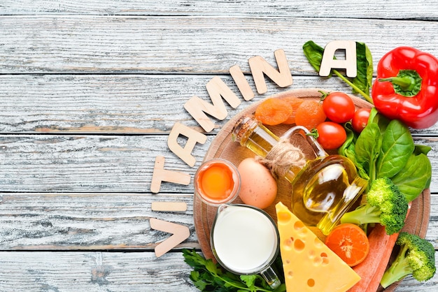 Voedingsmiddelen die natuurlijke vitamine A bevatten: broccoli, wortelen, melk, kaas, spinazie, abrikozen, peterselie, tomaten. Op een witte houten achtergrond. Bovenaanzicht.