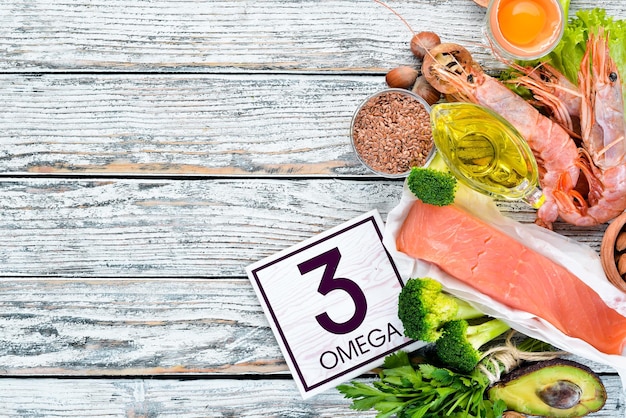 Voedingsmiddelen die omega-3 vitamine bevatten Gezonde voeding avocado's vis garnalen broccoli vlas noten eieren peterselie bovenaanzicht vrije ruimte voor uw tekst op een witte houten achtergrond