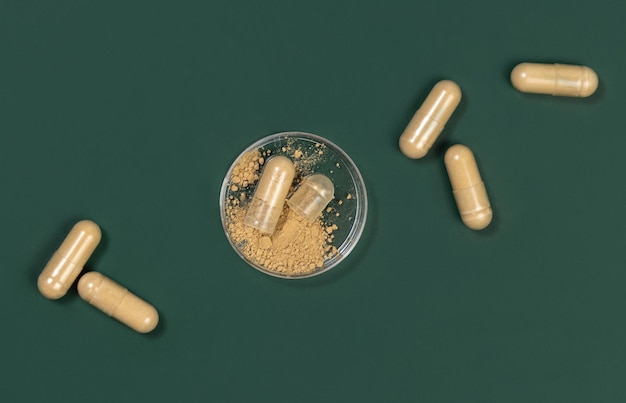 Foto voedingssupplementencapsules op donkergroen topweergave. eén capsule geopend om beige poeder in een pot te laten zien. preventieve geneeskunde en gezondheidszorg, het nemen van vitamines. farmaceutisch product