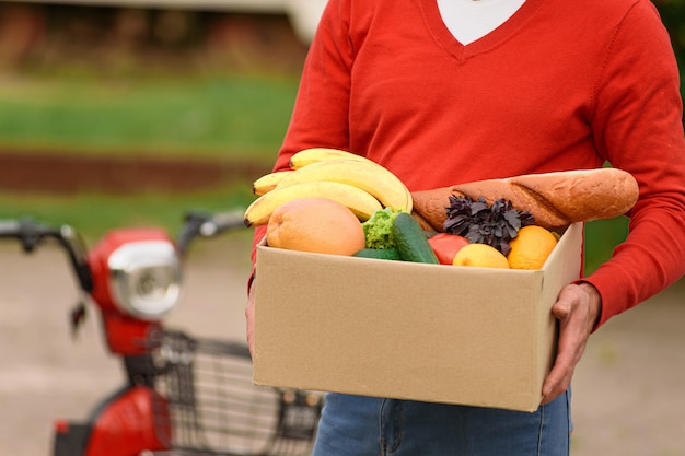 Foto voedsel bezorger in rood uniform met een cortondoos met boodschappen in zijn handen