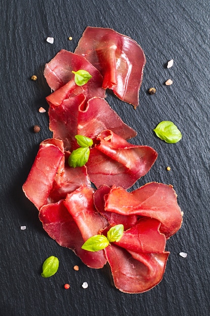 Voedsel concept Gesneden gedroogde Cured beefs Bresaola op zwarte leisteen stenen bord