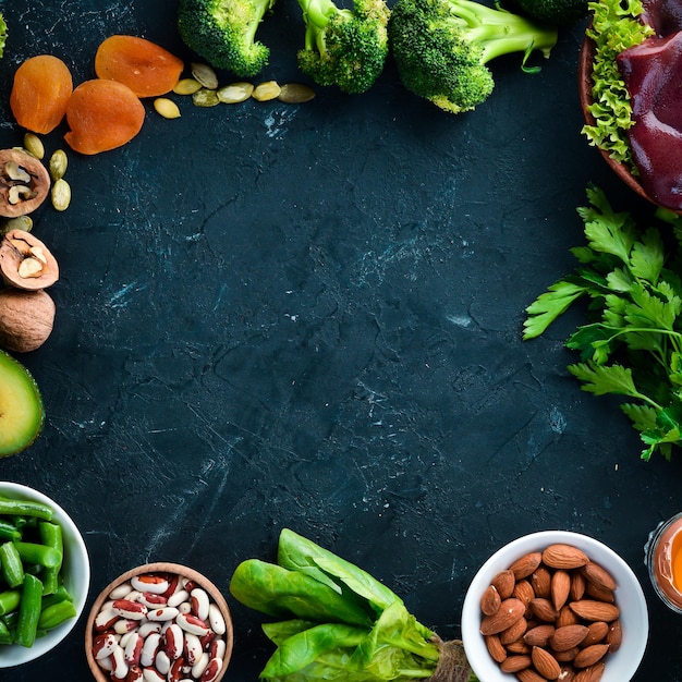 Voedsel dat natuurlijk ijzer bevat Fe Lever avocado broccoli spinazie peterselie bonen noten op een zwarte stenen achtergrond Bovenaanzicht