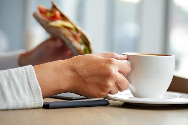 voedsel, diner en mensenconcept - vrouw die koffie drinkt en panini-sandwich eet voor ontbijt of lunch in café