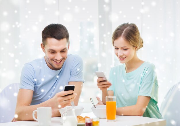 voedsel, familie, mensen en technologieconcept - glimlachend paar met smartphones en thuis ontbijten