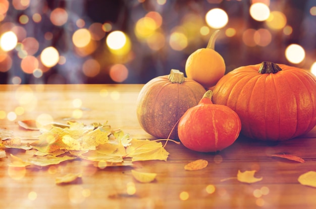 voedsel, halloween, oogst, seizoen en herfstconcept - close-up van pompoenen en bladeren op houten tafel over vakantielichten