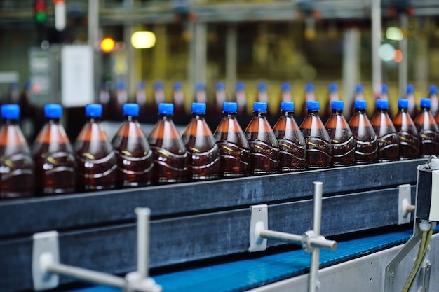 Voedsel industriële productie van bier. Plastic bierflesjes op een transportband tegen de achtergrond van een brouwerij.