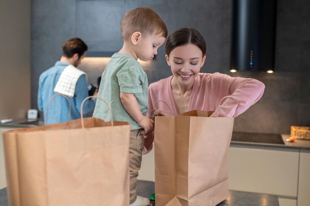Voedsel. jonge moeder met een klein kind dat zakken met eten opent in de keuken