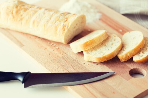 voedsel, junkfood, dieet en ongezond eten concept - close-up van wit brood of stokbrood en keukenmes op houten snijplank